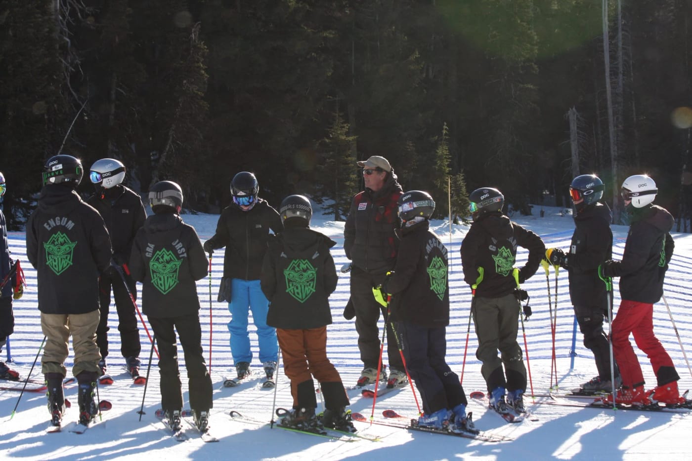 The team side by side on corduroy at a morning course inspection, low sun through the trees behind